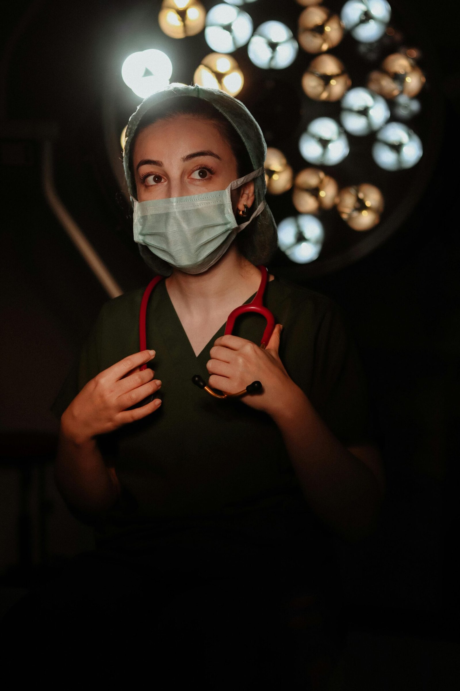 Nurse in scrubs with stethoscope in a dimly lit operating room setting