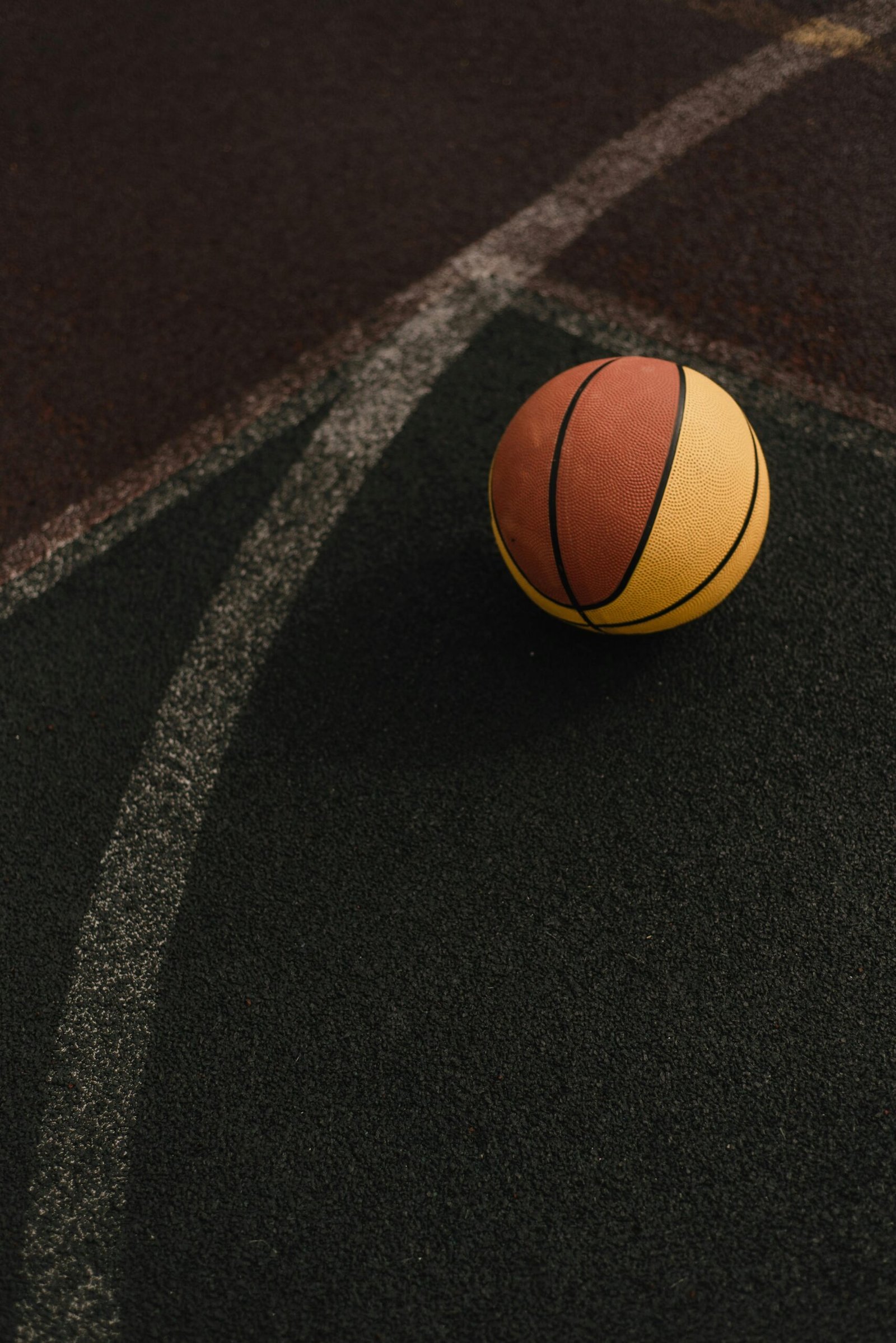 A lone basketball rests on an outdoor court featuring curved yellow lines.