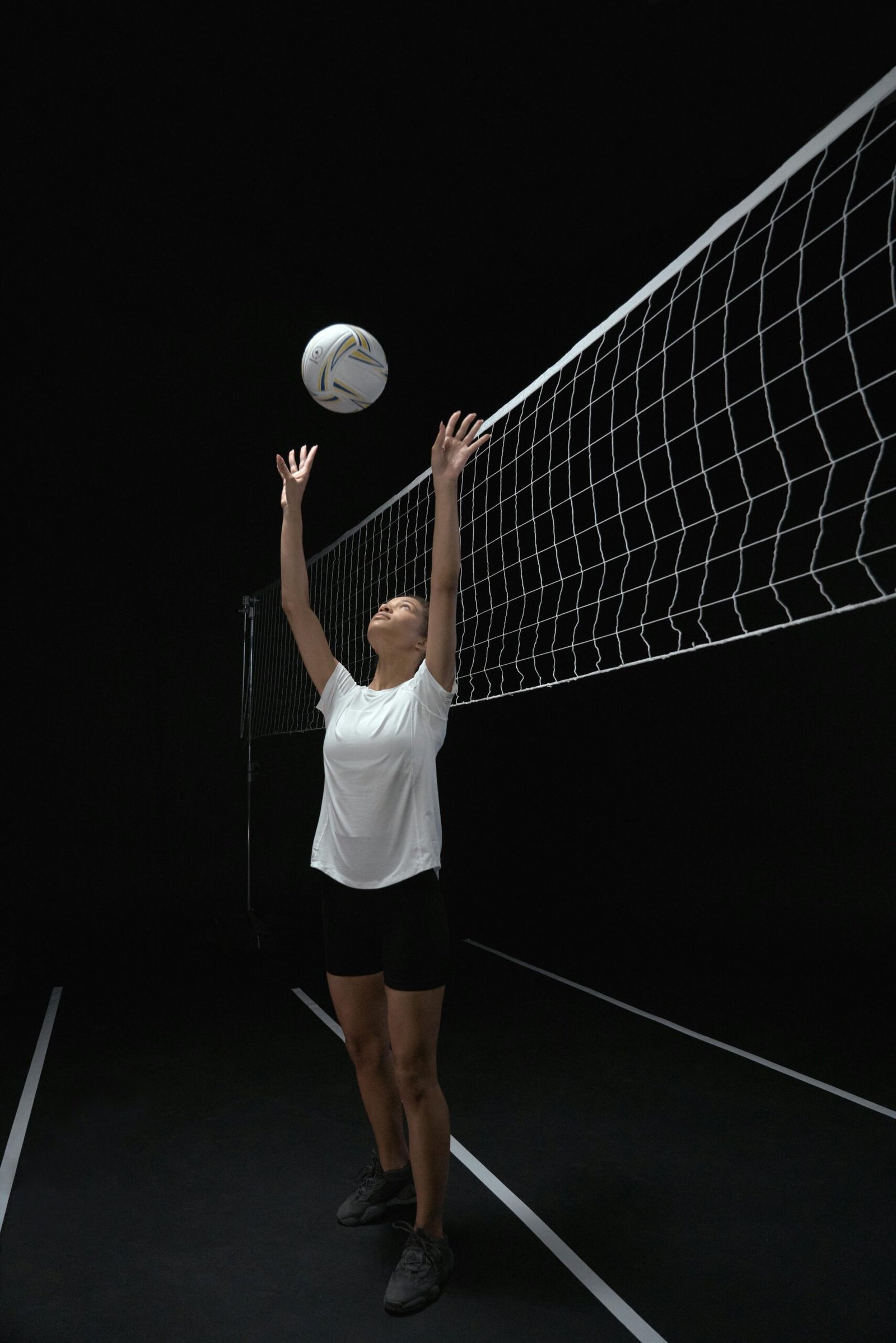 Athletic woman playing volleyball indoors, set against a dark background in a dynamic action shot.